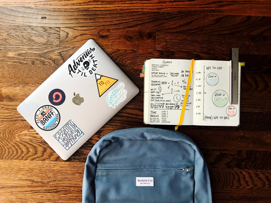 Backpack, laptop and open note book on a wooden surface