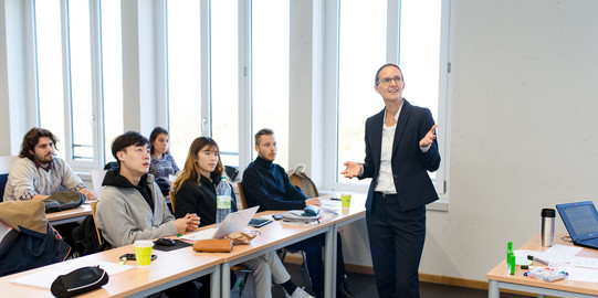 Dozentin steht vor einer Gruppe von Studierenden.