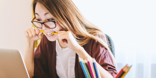 Photo: Woman looking at her laptop screen, nervously chewing on a pencil