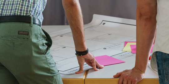 Foto Brainstorming Foto von zwei Personen, die sich mit den Händen auf einen Tisch mit Plänen stützten