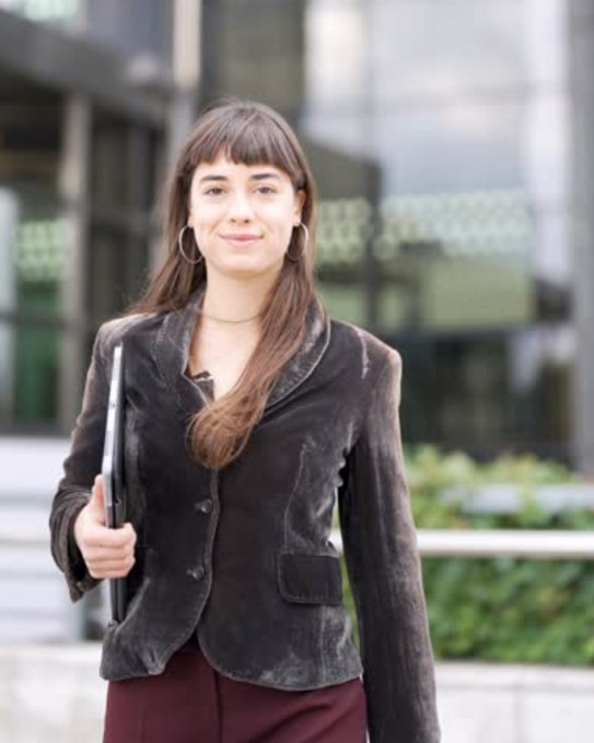 Frau mit Notebook im Arm vor modernem Gebäude mit Glaswänden