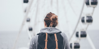 Frau mit Rucksack, von hinten fotografiert, vor Riesenrad
