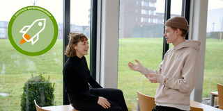 Junge Frau und junger Mann besprechen etwas vor dem Fenster. Logo Zertifikat Entrepreneurship oben in der Ecke.