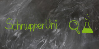 Grafik SchnupperUni Mit grüner Kreide auf nicht ganz sauber gewischter Tafel geschriebener Text "SchnupperUni" , daneben eine gemalte Lupe und ein halb gefülltes Reagenzglas