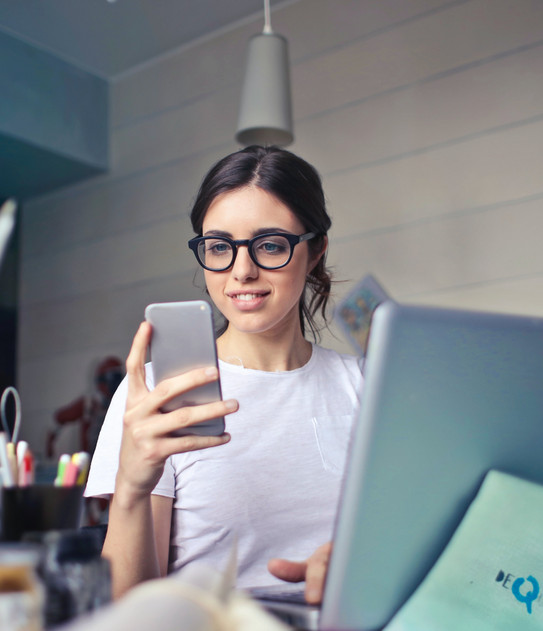 Foto: Frau blickt auf Handy in ihrer Hand, vor Schreibtisch mit Stiften und Laptop