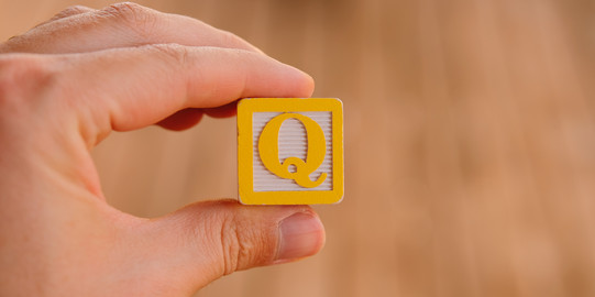 Foto: Hand, die ein Quadrat mit dem Buchstaben Q in der Mitte hält.