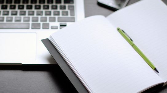 Laptop und Notizbuch Laptop und Notizbuch mit Stift auf einem Tisch liegend.