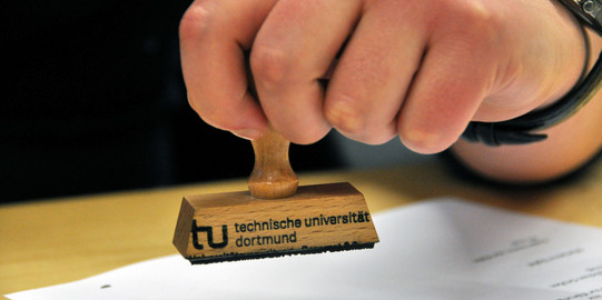 Symbolbild Stempel Nahaufnahme einer Hand, die einen Stempel der TU hält.
