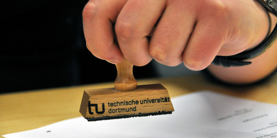 Symbolbild Stempel Nahaufnahme einer Hand, die einen Stempel der TU hält.
