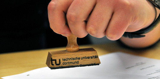 Symbolbild Stempel Nahaufnahme einer Hand, die einen Stempel der TU hält.