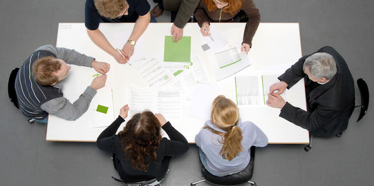 Besprechungssituation Studenten und Professoren Studierende und Dozierende sitzen gemeinsam an einem Tisch und arbeiten.