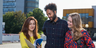 Studierende am Campus Nord Drei Studierende stehen zusammen auf einem Platz vor zwei Gebäuden.