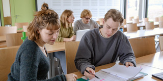 Studierende Tutorium Panorama Vier Studierende sitzen im Seminarraum. Zwei sitzen im Vordergrund und arbeiten zusammen.