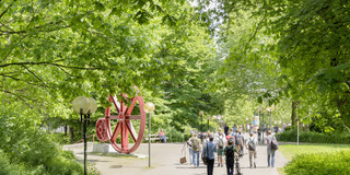 Students are on the North Campus in the summer, red gears in the background. 